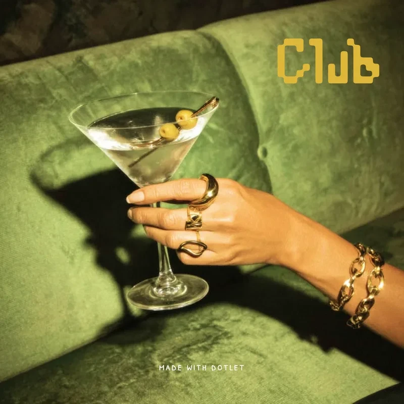 The Club wordmark in mustard over a photograph of a hand holding a martini against green velvet.